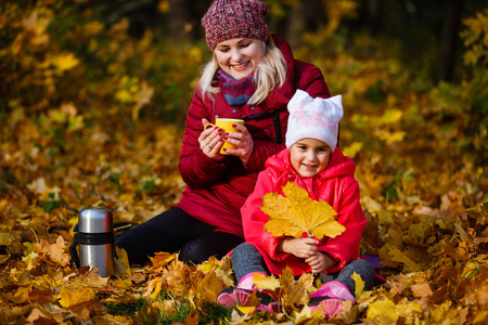 妈妈和女儿在秋天公园喝热水瓶里的茶