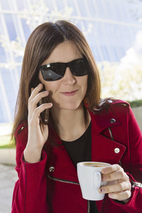 一个年轻的女人喝咖啡，用手机