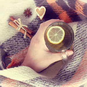 在温暖的毯子背景下，手拿着一个透明的杯子里的柠檬茶，在舒适的氛围中观看周末会议
