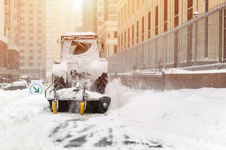 拖拉机用刷子和铲子清理城市街道上的雪，并在冬天大雪后停车。