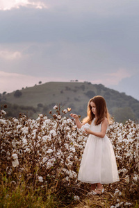 美丽的小女孩留着长发，穿着白色的连衣裙在田里。
