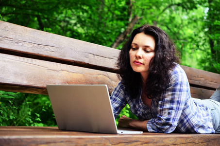 在公园里用笔记本电脑旅行的女人。从事自然工作的自由职业概念