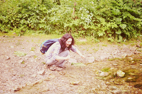 旅行的女人在森林里用溪流中的水洗脸和洗手。女孩坐在背包里