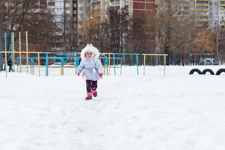 穿着蓬松外套的小女孩在雪地操场上玩耍
