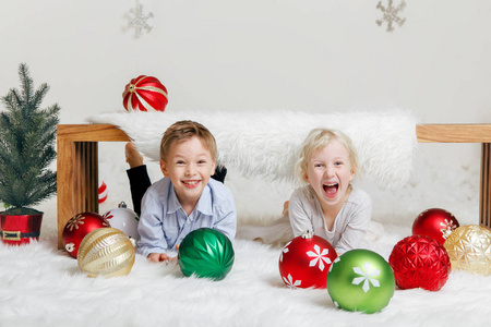 白人白种人儿童朋友的肖像躺在木凳下笑着庆祝圣诞节或新年。 小可爱的可爱男孩和女孩在画室里玩节日装饰