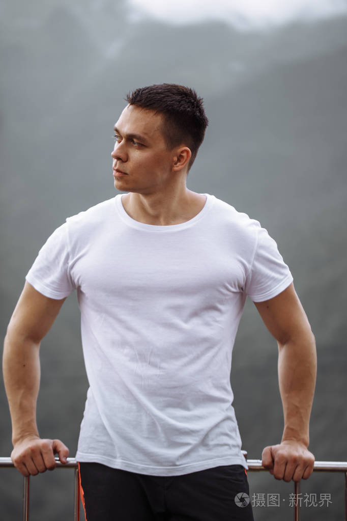 英俊的肌肉驼背男人看着高地的风景从山顶上看着雾蒙蒙的天空感觉到