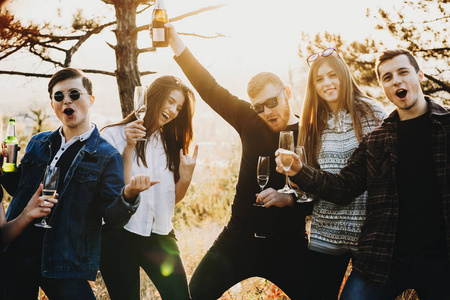 举酒杯一群有魅力的年轻人举着酒杯和酒瓶,一边喝酒,一边大喊大叫,站