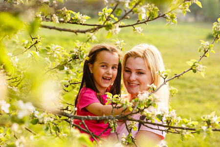 年轻母亲在绿树旁牵手女儿的画像