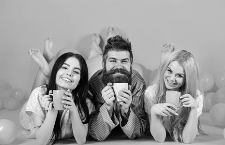 恋人在床上喝咖啡 三人早上用咖啡放松 暴风雨夜的概念 男人和女人穿着家用衣服 睡衣 男人和女人 在昏昏欲睡的面孔的朋友躺在 照片 正版商用图片0r02c5 摄图新视界