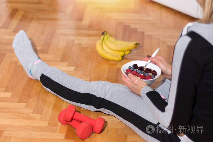 早上的女孩坐在地板上锻炼后在碗里吃燕麦粥地板上有红色的哑铃和香蕉
