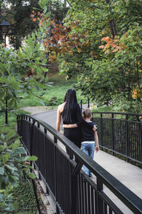 孩子抱着他的妈妈，在一个五彩缤纷的秋天背景的公园里走过桥