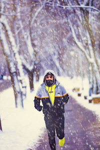 男人在下雪的公园和寒冷的天气慢跑。