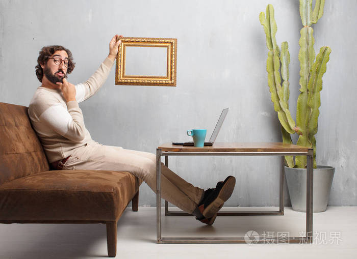 坐在老式客厅里的皮革沙发上的一个留着胡子的年轻人