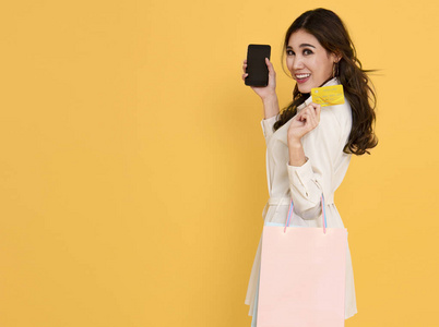 亚洲女性购物者使用手机和信用卡付款。 黑色星期五和购物在线概念孤立在黄色背景。