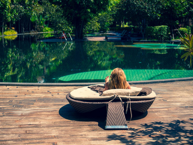 美丽的女人坐在池边，看着池中的绿松石水，在巴厘岛的豪华海滩度假胜地度过暑假