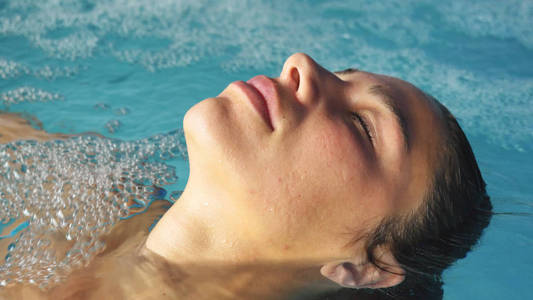 美丽的年轻女孩女人在蓝色背景下穿着蓝色泳衣的水疗浴中放松。 概念水疗程序，身体按摩，水疗，奶油，放松，水疗，水处理，游泳池