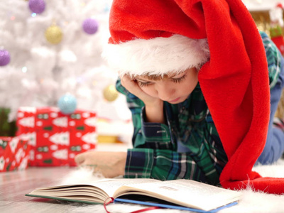 戴着长长的圣诞帽的男孩在圣诞树附近看书