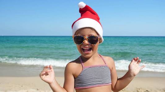 一个小女孩正在海上玩，戴着圣诞老人的帽子，穿着泳衣，戴着太阳镜，背景是深蓝色的海水。