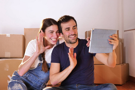 夫妻俩在新公寓房间里用数字平板电脑躺着，纸板箱挥舞着手