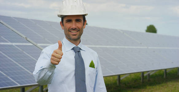 商人站在生态太阳能电池板屋顶电池太阳能系统站时竖起大拇指