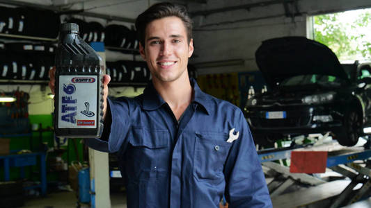 在机械师中，一名机械师在检查了汽车上的油和发动机后，微笑着显示了使用的油箱。 概念安全保险和专业修订。