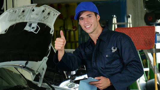 在车库里，一个机械师在检查和完成机器后，他的拇指向上和微笑，因为汽车已经修理成功了。 概念安全保险。