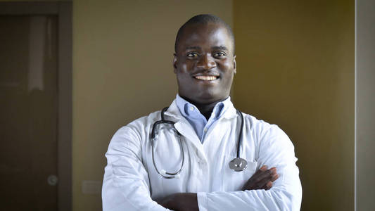 成功的医生微笑(非裔美国人)白色牙齿白色外套听诊器棕色眼睛棕色背景