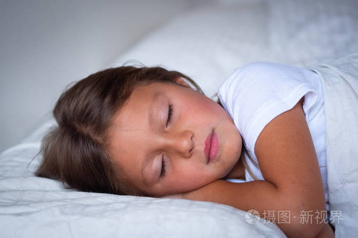 一个美丽的女孩睡觉,在她铺着毯子的白色床上做着安静的梦.
