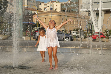 两个小女孩玩得很开心,在喷泉里玩,笑着穿着白色衣服,背景是透明的水.