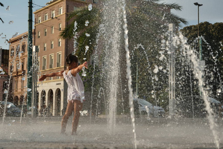 美丽的小女孩玩得很开心，在喷泉里玩，微笑着穿着透明水的白色裙子。