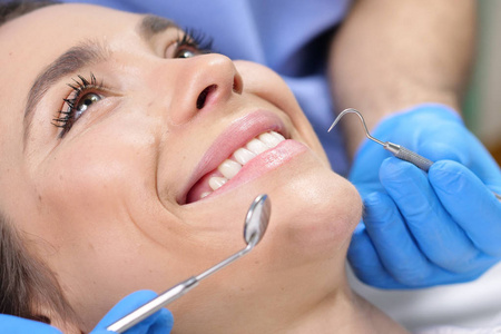 在一个专业的实践中，一位牙医检查病人的牙列，她对来访感到高兴，微笑着显示出完美的白色牙齿。 概念牙医保健完美微笑。
