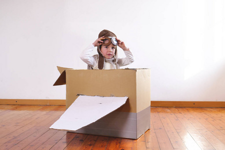 穿着飞行员服装的小男孩在家玩手工纸板箱飞机