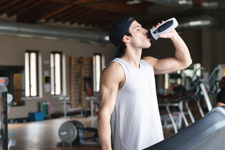男人在休息时从瓶子里喝水，而站在健身房