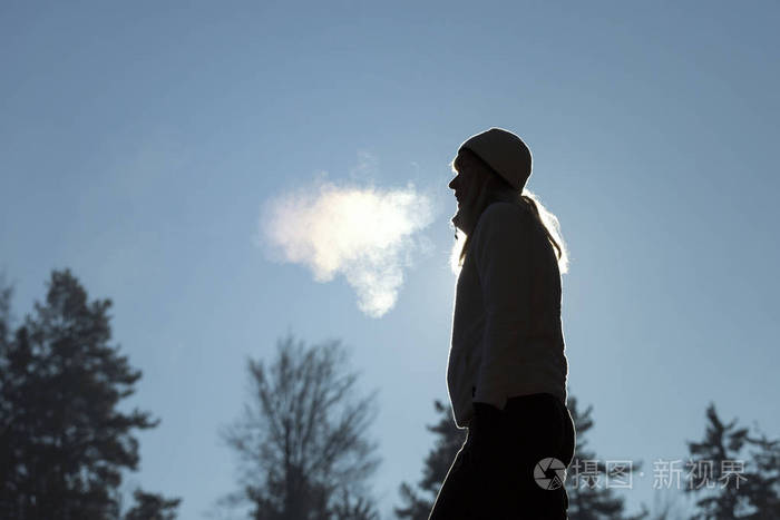 一个戴帽子的女人在寒冷的冬天早晨呼吸温暖的空气的轮廓.