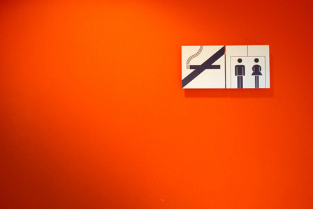 禁止吸烟和带有橙色墙壁背景的厕所标志