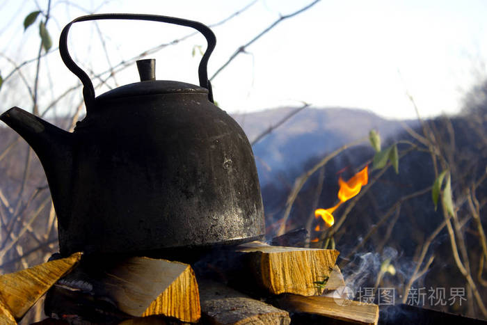 在大锅里露营做饭，在火上喝凉茶。一个人在天晴的时候在大锅里准备食物。在水壶和火盆里野餐时吃的。