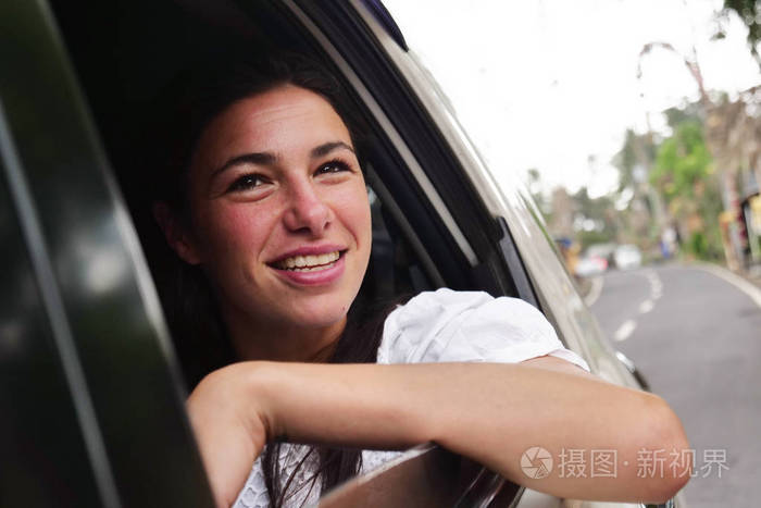 在一个阳光明媚的日子里,一个美丽的女人把旅行的头放在车窗外,欣赏