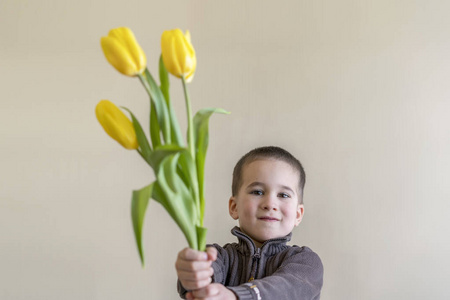 带着一束黄花的小男孩。 男孩把花藏在手上。 光线背景。 欧洲外观