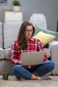 一个微笑的女性戴着眼镜，使用笔记本电脑，在家里的沙发上放松。