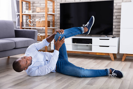 一个年轻的非洲男人在摔倒在地后抱着受伤的膝盖照片