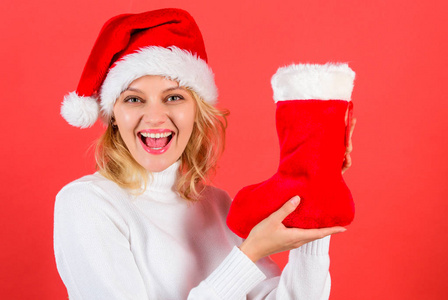 女孩开朗的脸得到了礼物在圣诞袜子。检查圣诞长袜的内容。传统的寒假。夫人在圣诞老人帽子举行圣诞礼物红色背景。圣诞长袜概念