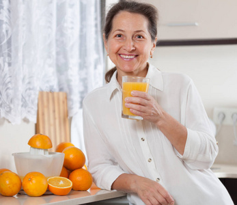 微笑的中年妇女在厨房准备橙汁