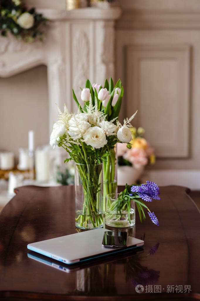 一束花放在一张靠近手机和笔记本电脑的桌子上放在优雅的简单花瓶里