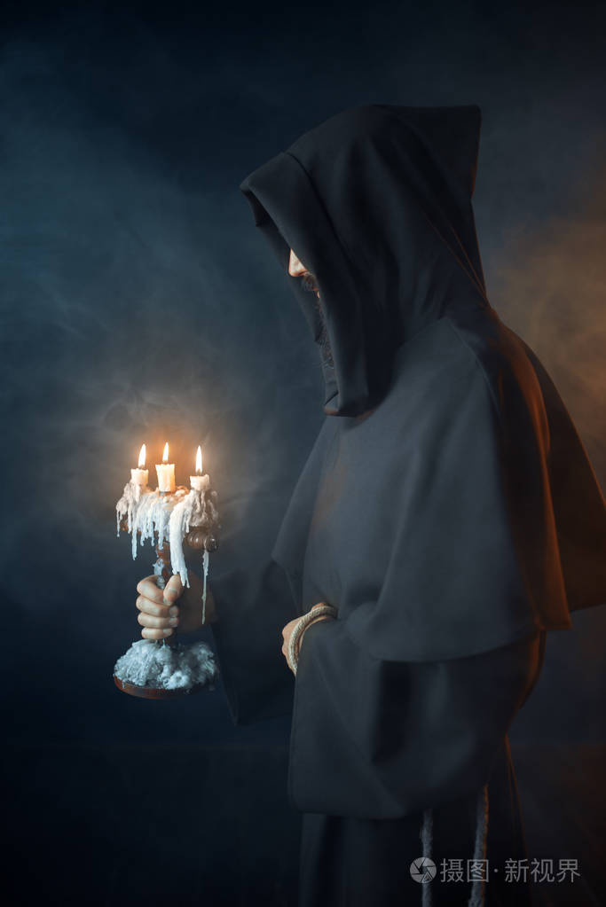 中世纪僧袍手持烛台黑色背景秘密仪式带蜡烛的神秘修士神秘与灵性