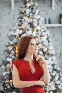 圣诞节。美丽的微笑的妇女优雅在圣诞树在红色礼服灯背景。新年快乐