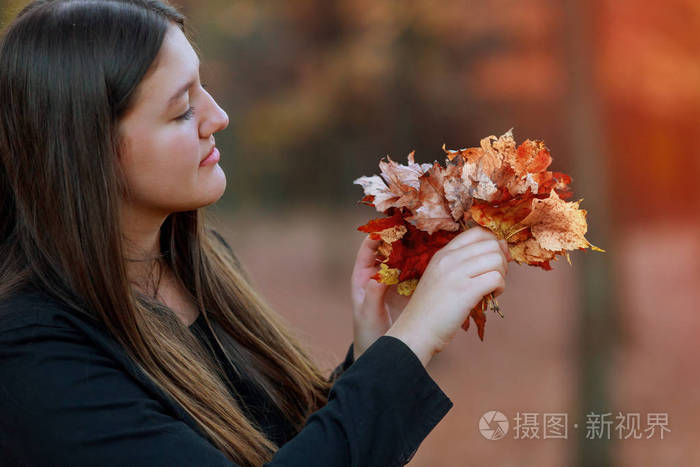 秋天美丽的肖像女孩在秋天公园里,手里拿着树叶.