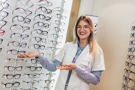 眼科诊所有吸引力的年轻女医生。 医生眼科医生正站在不同眼镜的架子附近。