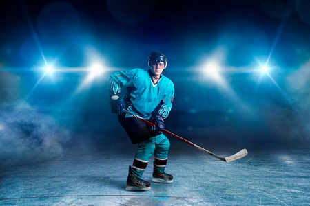 一名冰球运动员在冰场滑冰，黑色背景的聚光灯。戴头盔戴手套穿制服的男性手拿棍子