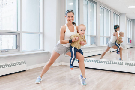 有孩子的年轻女子在体育课上锻炼以减轻婴儿体重。适合有幼儿的母亲的儿童健身。父母活动的生活方式概念。
