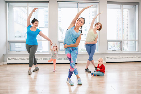 三组年轻女性带着孩子在体育课上锻炼，教练指导放松婴儿体重。适合有孩子的母亲的儿童健身。父母活动的生活方式概念